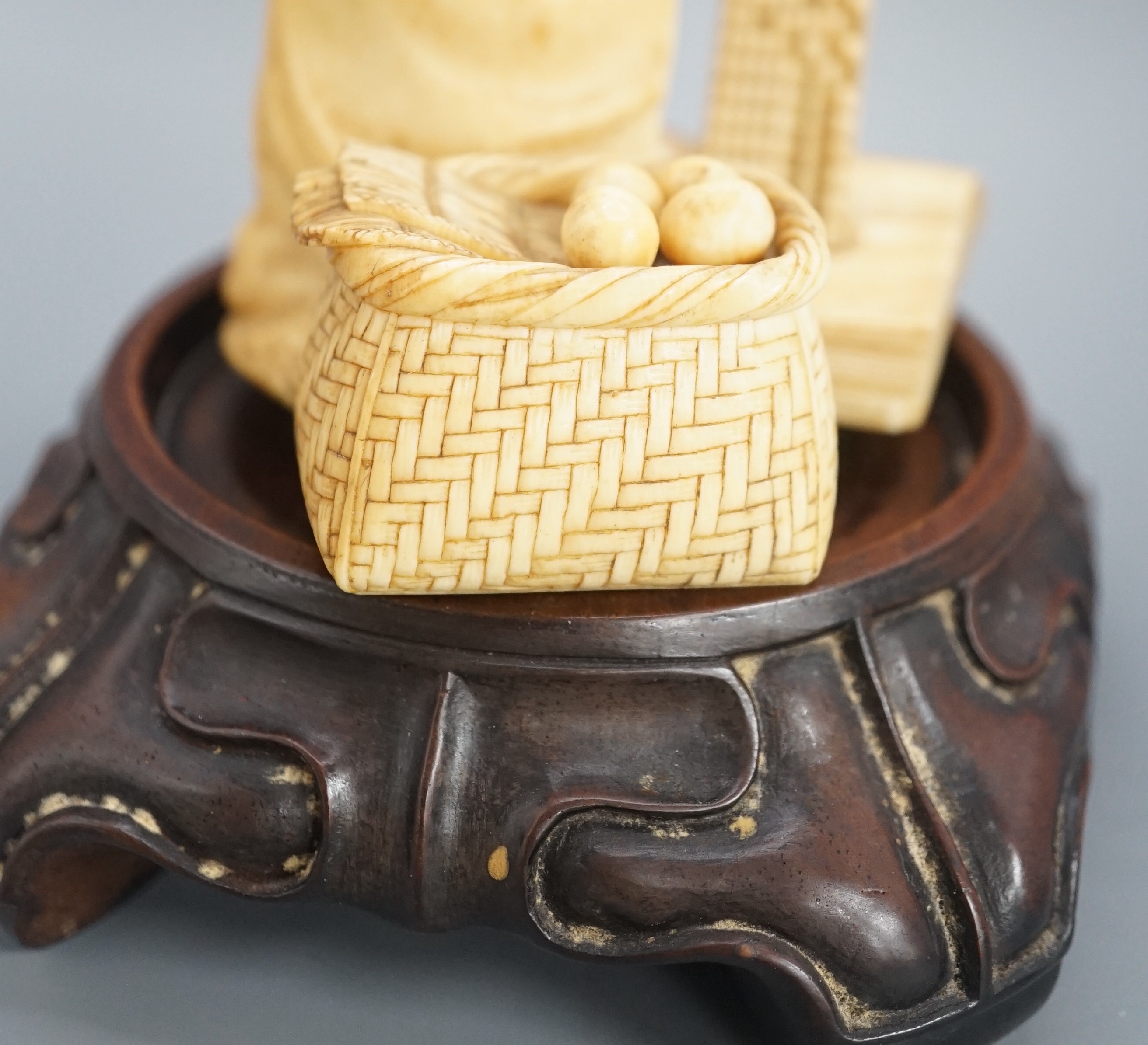 A Japanese ivory okimono of a street vendor kneeling and holding an abacus, Meiji period, 8cm, associated wood stand